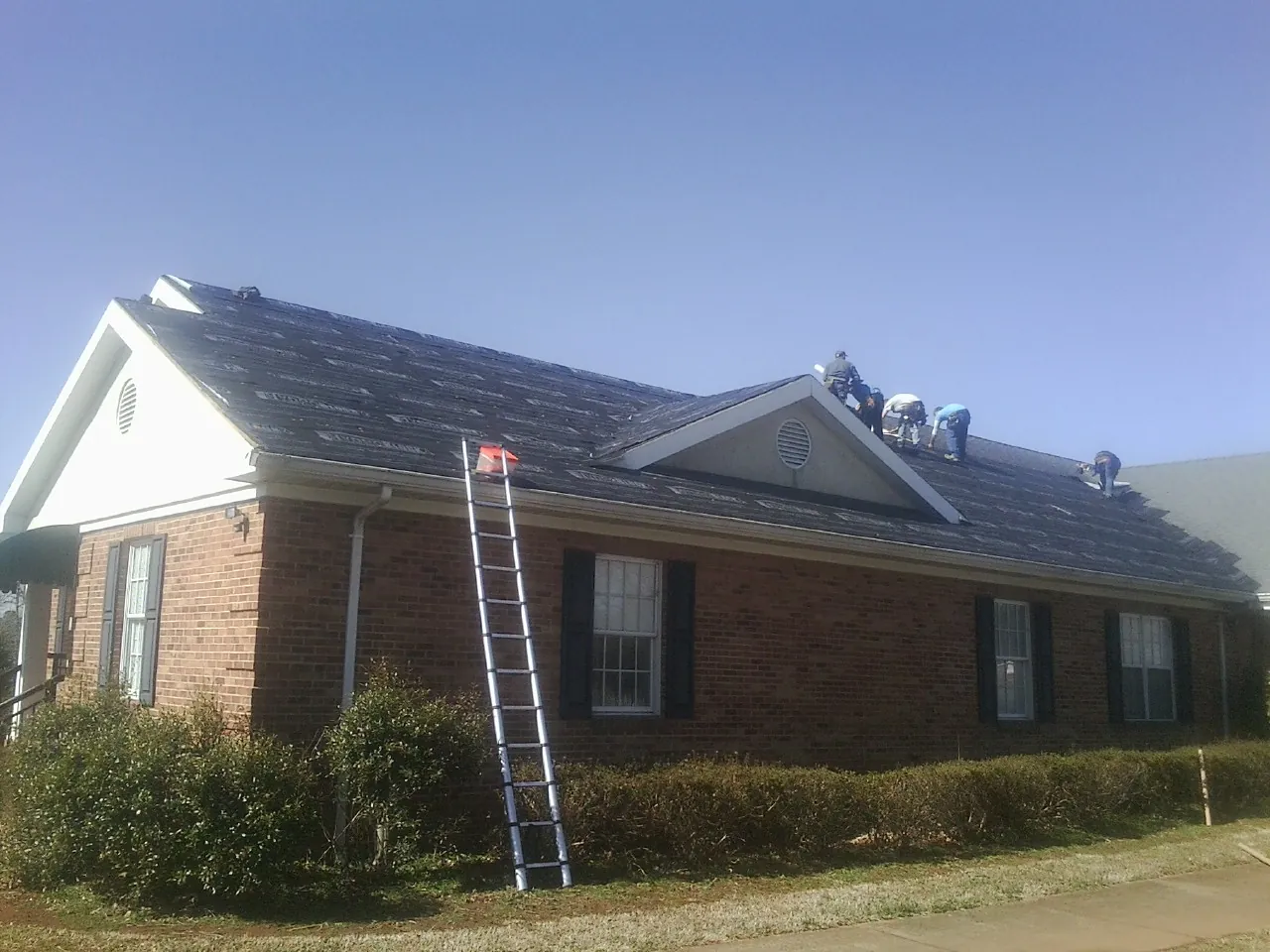 Crew tearing shingles off a brick ranch roof with a ladder set — Emergency Roof Repair work by our crew in Cupertino