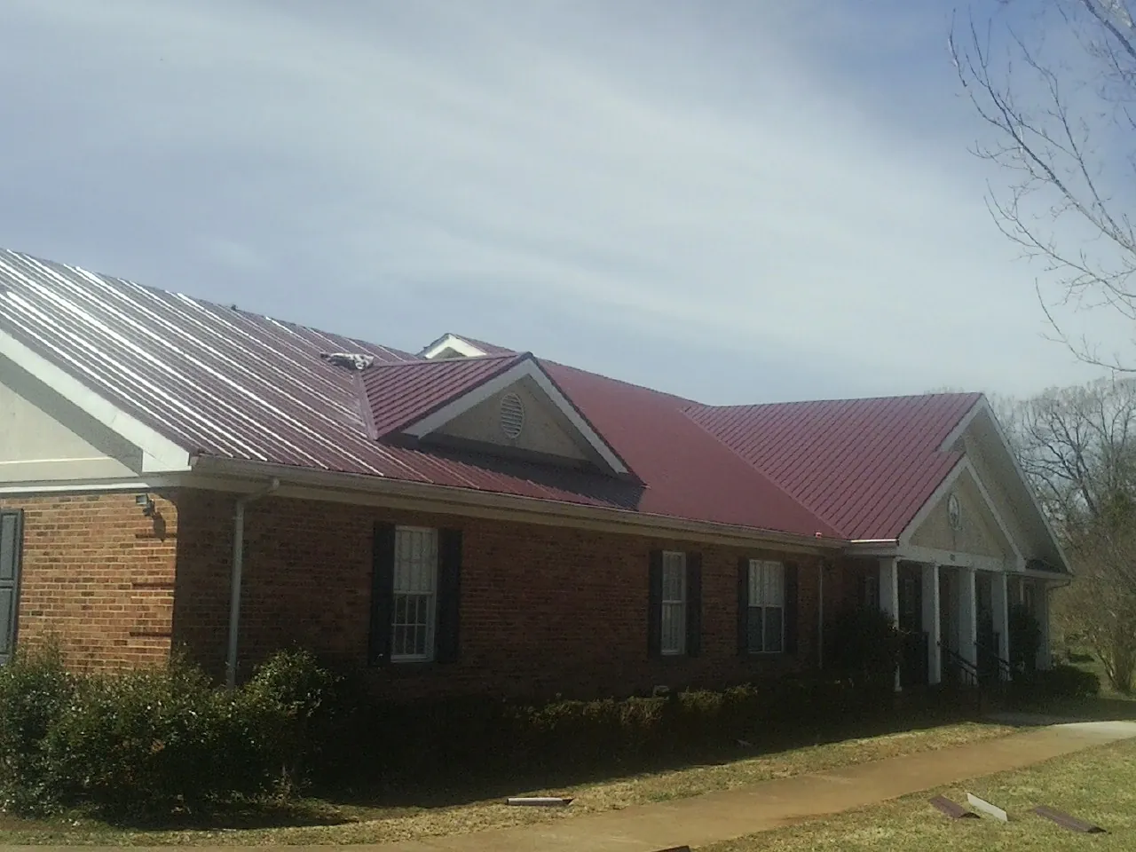 Red metal roof with gabled entries on a long brick building, from a Hail Damage Roof Repair job in Cupertino