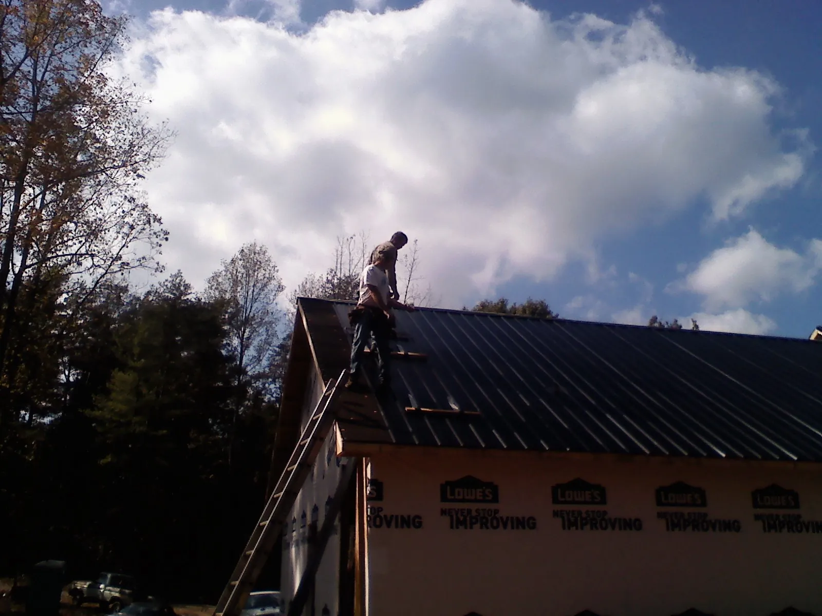 Roofer fastening dark metal panels high against a cloudy sky, from a Roof Inspection job in Cupertino