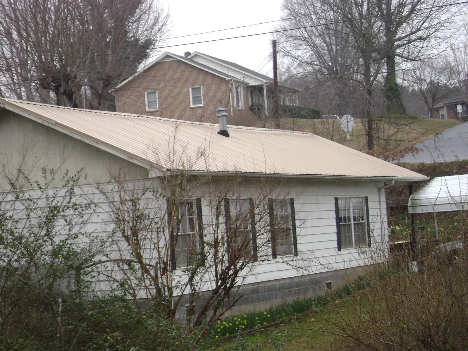 Tan metal roof on a white sided house set into a hillside — Commercial Roofing by Roofing Brothers in Cupertino